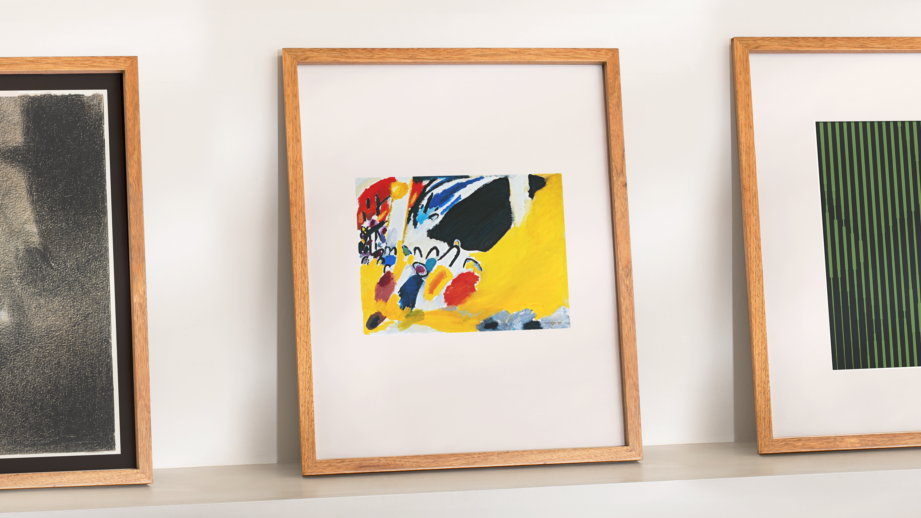 Three framed prints leaning against a white wall.